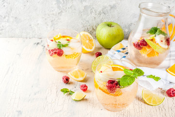 Summer cold cocktail, fruit and berry white sangria with apple, lemon, oranges and raspberry. light concrete background, copy space