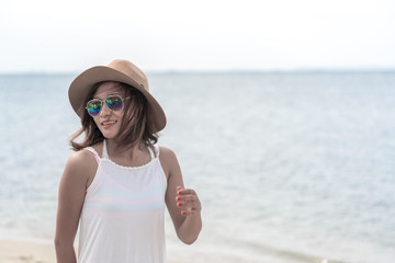 Smiling Asian young woman in white dress and cowboy hat on the beach