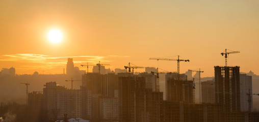 Panorama of sunset in the city with silhouette of buildings and industrial cranes