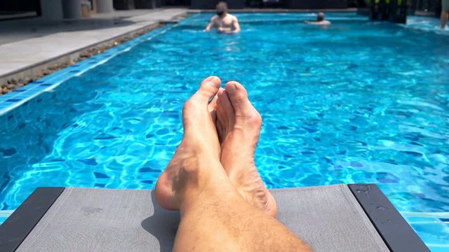 Male's legs lying on sunbed next to the pool, slow motion shot at 240fps
