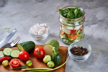 Delicious vegetable salad in jar and fresh veggies on cutting board on white background, selective focus, close-up