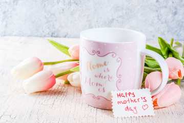 Mother's Day concept, greeting card background. Flowers tulips on a light concrete table, mug with inscription 