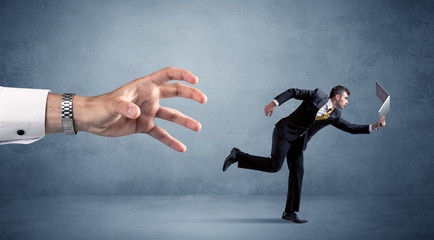 Young miniature businessman running from a big hand 