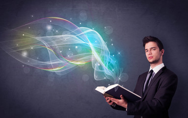 Casual young man holding book with rainbow waves flying out of it
