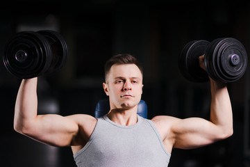 Fototapeta na wymiar Strong handsome fit man exercising in the gym. Personal trainer workout. Athletic man working out his chest with dumbbells on a bench press. Fitness, healhty lifestyle, bodybuilding concept.