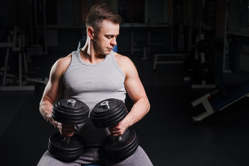 Fototapeta na wymiar Strong handsome fit man exercising in the gym. Personal trainer workout. Athletic man working out his chest with dumbbells on a bench press. Fitness, healhty lifestyle, bodybuilding concept.