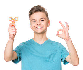 Young teen boy holding popular fidget spinner toy and making ok gesture. Happy smiling child...