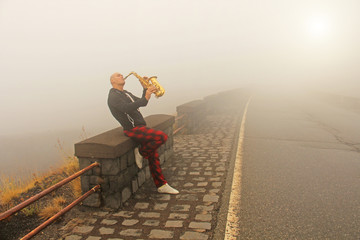 A bald man plays on a gold alto saxophone on the roadside, again