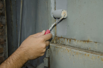 Mano de hombre pintando con rodillo pequeño. Superficie de chapa oxidada.