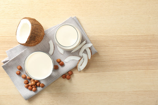 Glasses with milk substitute and nuts on wooden background, flat lay