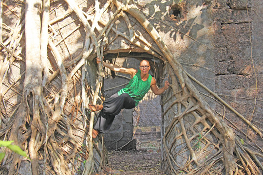 Red Fort in India, Goa. The saxophonist freak plays on a gold alto saxophone in an unusual place, among the old fort and tree roots