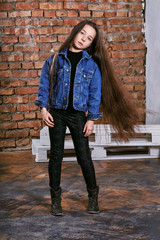 Girl teenager brunette,long beautiful hair posing in loft interior,brick wall.Young woman looking confident, casual clothing,jeans jacket,boots,pants.Photos for shop youth,showcase,advertisement.