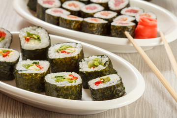 Sushi rolls with nori, rice, pieces of avocado, cucumber, red bell pepper and lettuce leaves on ceramic plate