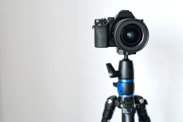 professional black mirrorless camera stands on a tripod against a white wall. Blogging and video...