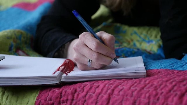 sed young woman lies on a bed and writes in her diary. adolescent experiences. slow motion