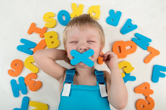 Happy charming Caucasian blond's kid in colored clothes playing with plastic letters. Learning the alphabet, preparing for school. Education for kindergarten and preschool children. White background