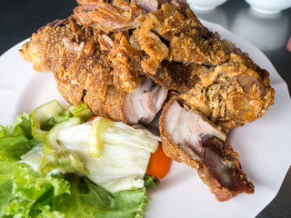 Crispy fried pork leg placed on a plate with vegetables and seasoning sauce