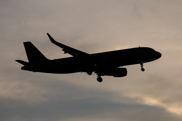 Silhouette passenger airplane flying away in to sky high altitude on sunset