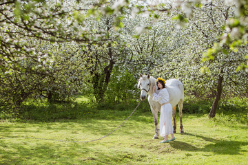 woman in national Ukrainian clothes with white horse in a flowery garden