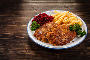 Grilled steak, French fries and vegetables on wooden background