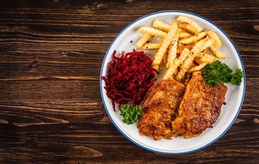 Grilled steak, French fries and vegetables on wooden background