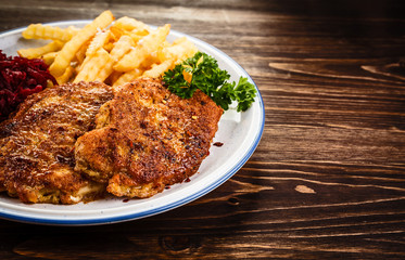Grilled steak, French fries and vegetables on wooden background