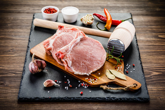 Fresh raw pork chops on black stone on wooden background