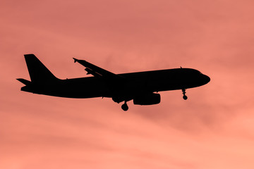 Silhouette passenger airplane flying away in to sky high altitude on sunset