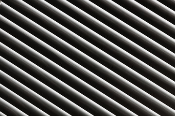 An abstract snapshot of a close-up illuminated grille that is angled with a dark background for patterns and backgrounds.