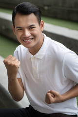 excited man, happy smiling positive man, man showing guts pose; portrait of excited happy smiling strong winning man raising his arms, looking up at you; southeast asian male model