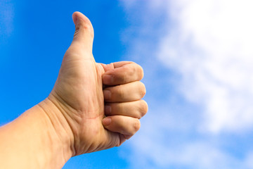 Male hand against a blue sky with clouds