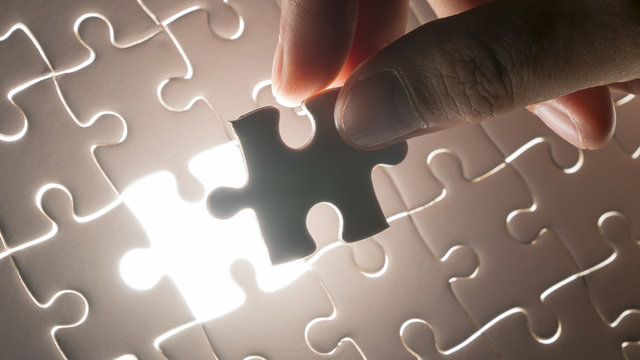 hand holding piece of white jig saw puzzle place to match or completing the final pazzle piece.Success,game,solve problem business concept.