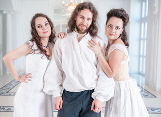 Handsome man in medieval costume and two woman in old-fashioned negligee