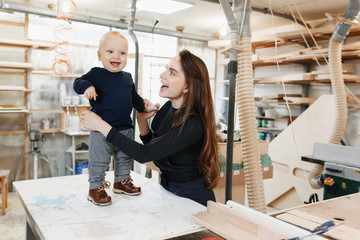 happy young mother with the little son in the carpenter workshop their father . Family business.