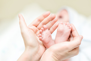 Mother holding feet of newborn baby. Infant legs in parent  hand. Child support  and care. Happy family