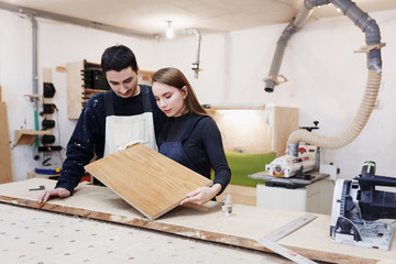 young happy family standing at a work bench in a carpentry workshop, process a tree a varnish. Family business. startup business. young specialist designer.