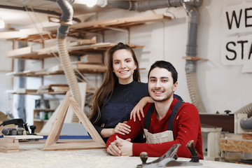 young happy family standing at a work bench in a carpentry workshop, writing a project. Family...