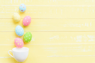 Fototapeta na wymiar Happy easter! Row colorful Easter eggs spread out from white cup on bright yellow wooden background.