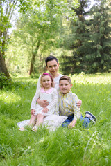 Fototapeta premium happy family outdoors on the grass in a park. mom and two children smiling