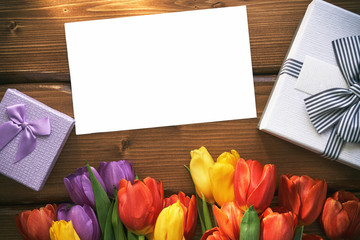 Blank paper card mock up with a gift box and tulips on a wooden table