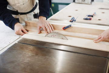 profession, carpentry, woodwork and people concept - two carpenters with electric drill drilling wood plank at workshop