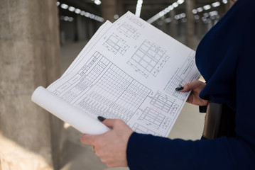 Naklejka premium Woman engineer with blueprints in hand, close-up. Building site. Business woman. In a black skirt and blue cardigan.