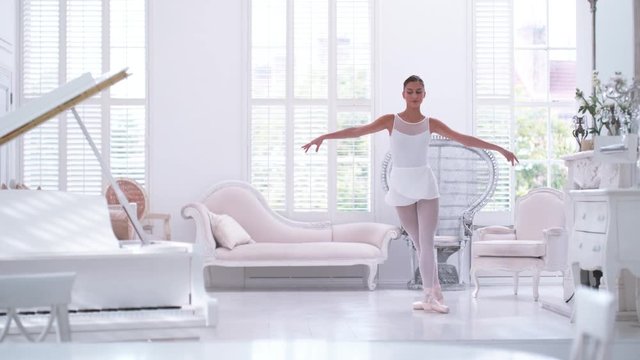 Graceful ballerina practicing ballet in white studio, slow motion