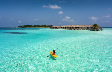 Frau im Kajak paddelt über die türkise Gewässer der Malediven © moofushi