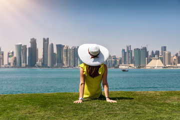 Attraktive Frau mit Sonnenhut sitzt auf einem Hügel vor der Skyline von Doha, Katar