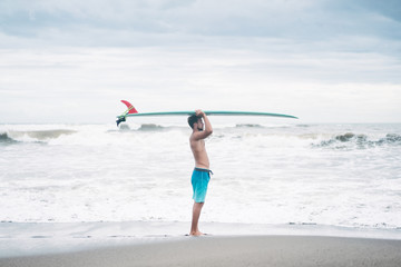 side view of surfer standing with surfboard on head in Bali, Indonesia