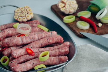 Raw gourmet sausages with fresh herbs, leek and chilli pepper spices on white table.