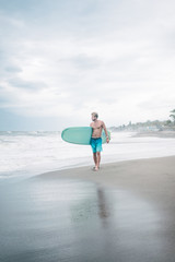 Fototapeta na wymiar handsome surfer standing with surfboard and looking at ocean in Bali, Indonesia