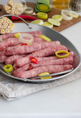 Raw gourmet sausages with fresh herbs, leek and chilli pepper spices on white table.