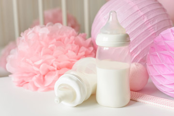 Baby bottles with breast milk with various festive paper decor and balloons in front of baby bedroom. It's a girl or baby birthday celebration concept. Baby shower concept.